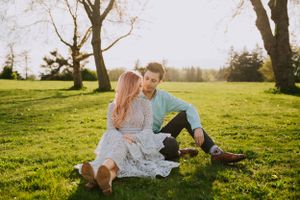 Couple relaxes on blanket in sunny park during golden hour surrounded by bare trees.