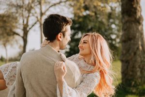 Couple shares intimate dance pose outdoors with pink hair flowing in evening light.
