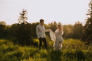 Couple dances together on hilltop meadow at sunset surrounded by evergreen trees.