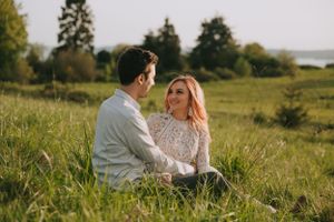 Two people sitting intimately in a grassy field during sunset with trees in the distance.