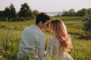 A tender moment captured between two people sitting in a sunlit field with rolling hills behind them.