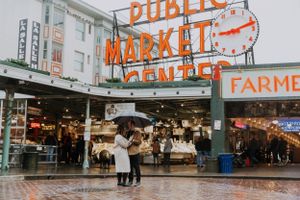 A couple with an umbrella standing in the rain at Pike Place Market in Seattle.