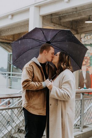 A romantic moment shared under a black umbrella on a rainy day.