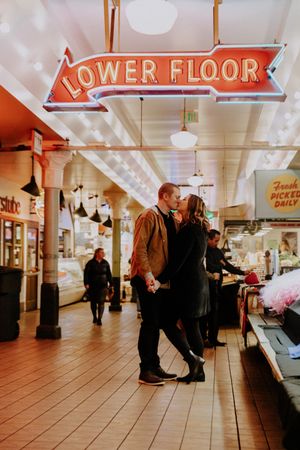 A couple sharing an intimate moment under a Lower Floor neon sign in a market hallway.