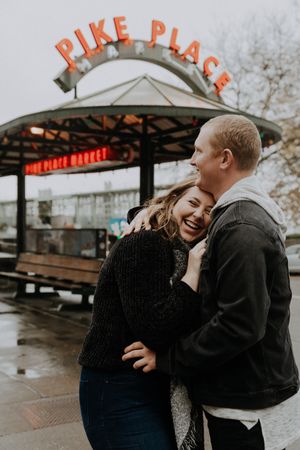 A couple sharing a laugh under the iconic Pike Place Market sign in Seattle.