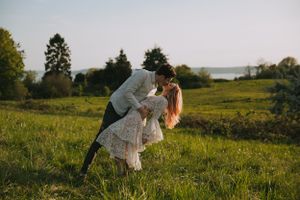 A tender kiss shared between a couple sitting in tall grass during golden hour.