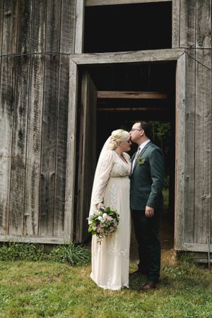 Wedding couple embracing in vintage barn doorway with elegant bouquet.