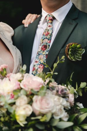 Floral tie and boutonniere detail with elegant wedding bouquet.