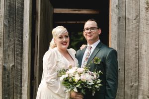 Happy newlyweds posing in rustic barn doorway with wedding bouquet.