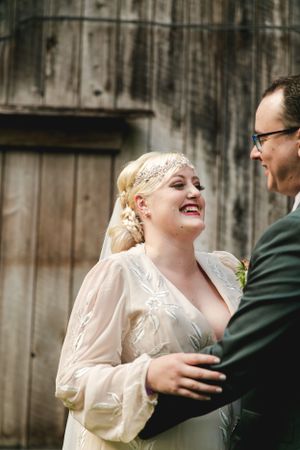 A joyful wedding moment shared between a bride in a vintage-style dress and her partner against a rustic barn backdrop.