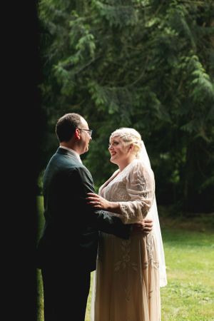 An intimate moment between newlyweds standing near evergreen trees during their wedding day.