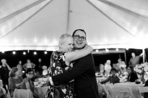 A heartfelt dance moment captured in black and white under an elegant wedding reception tent.
