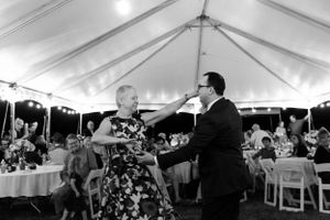 A playful dance captured at a wedding reception under a white tent with tables in the background.
