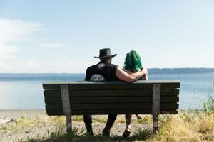 A couple sits together on a wooden bench overlooking a serene waterfront view.