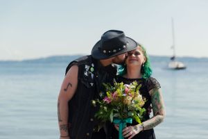 A couple shares an intimate moment by the ocean while holding a vibrant bouquet of flowers.