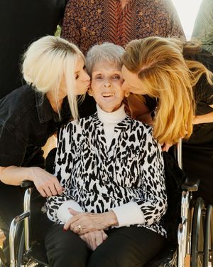 An elderly person in a wheelchair receives loving kisses from family members.