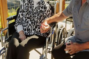 A close-up of hands holding together while sitting in a wheelchair.