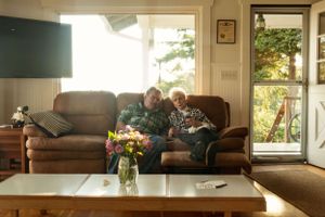 A cozy afternoon scene with two people on a brown couch reading together in a sun-lit living room.