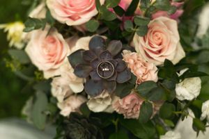 Wedding rings nestled among pink roses and succulent flowers in elegant bouquet.