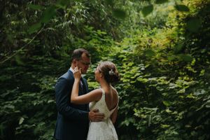 A wedding couple shares an intimate moment in a lush forest setting.