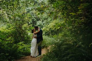 Couple embracing on forest path surrounded by lush greenery.