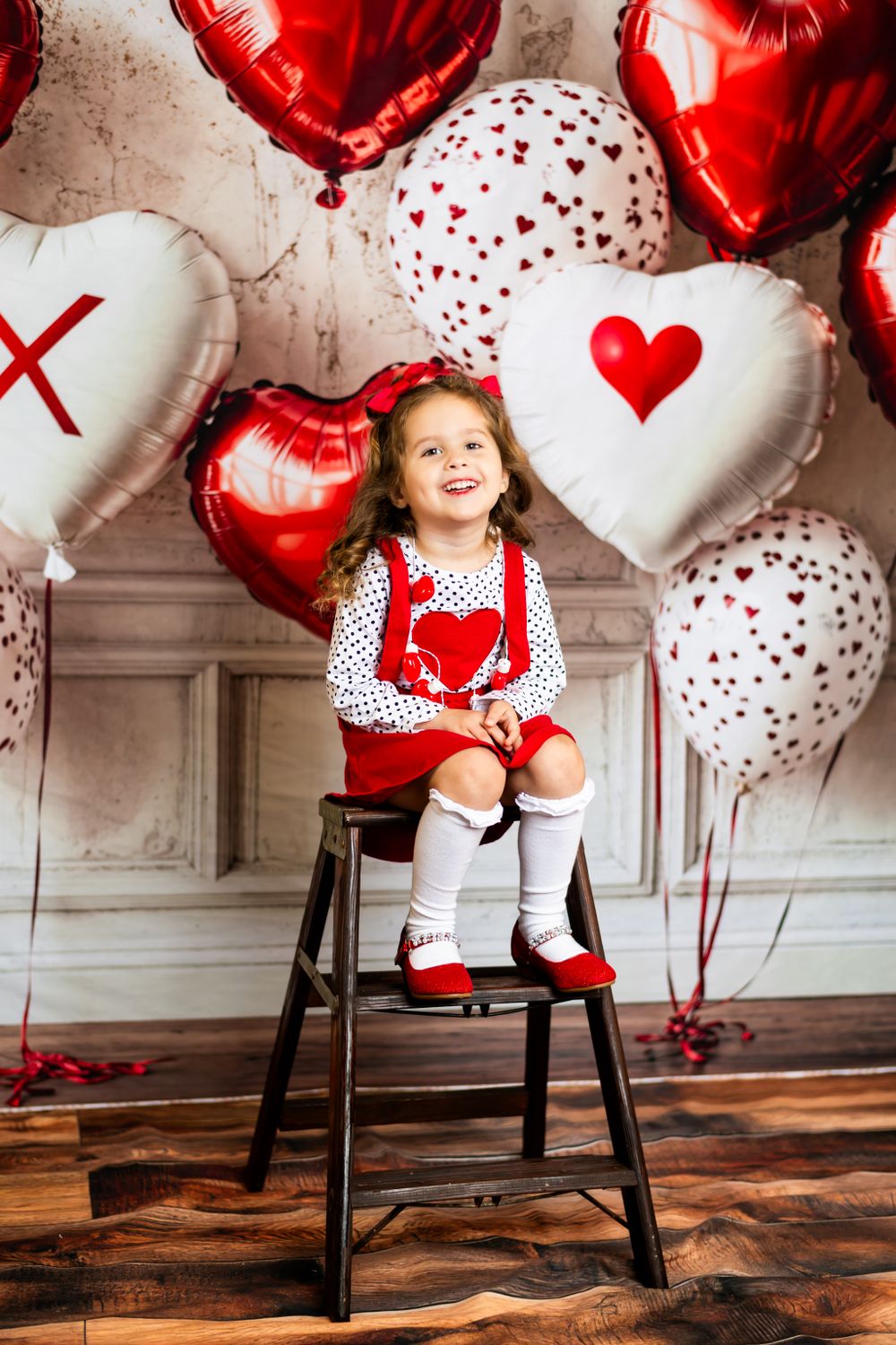 Valentine's Day themed decorations with red and white heart balloons, patterned dress, and wooden chair on rustic floor.