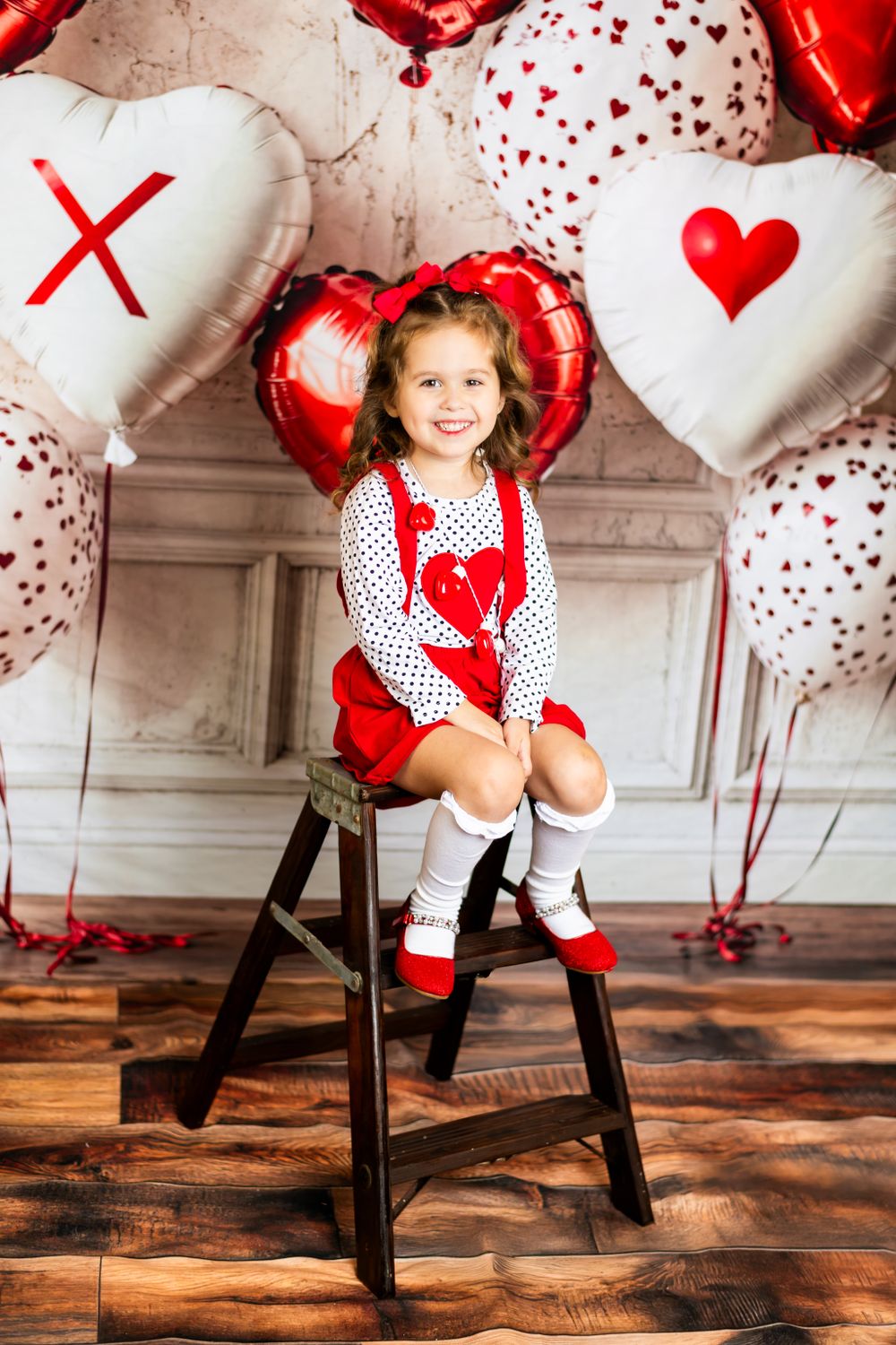 Valentine's day themed photo setup with red and white heart balloons and decorations on wooden floor with rustic backdrop.