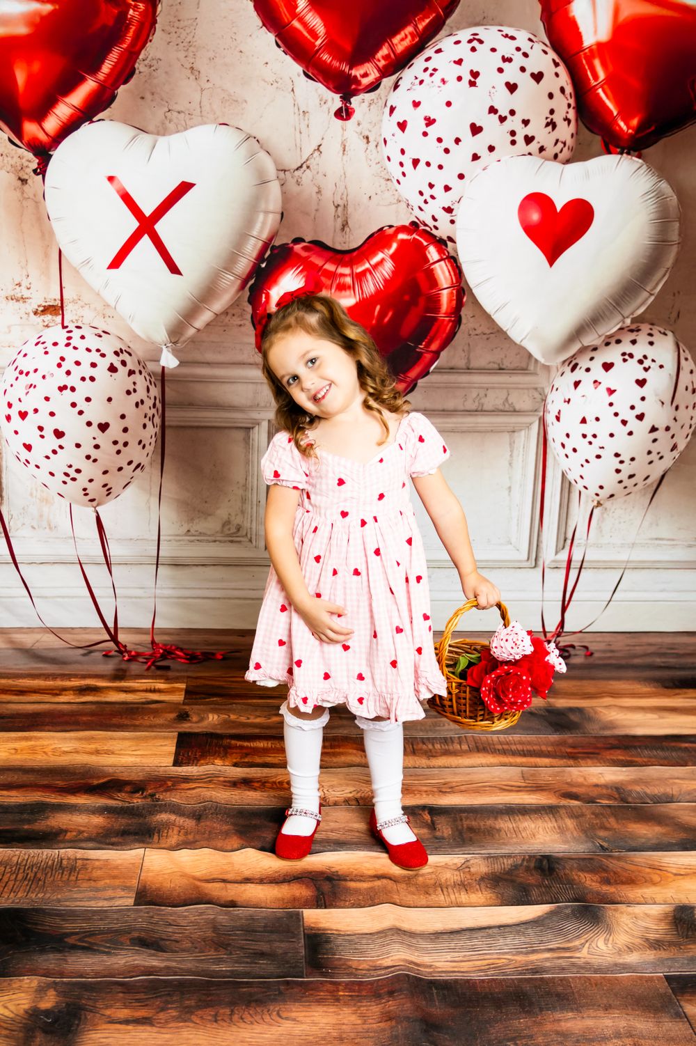 Valentine's themed photoshoot with heart balloons, red and white decorations, and wooden floor setting.