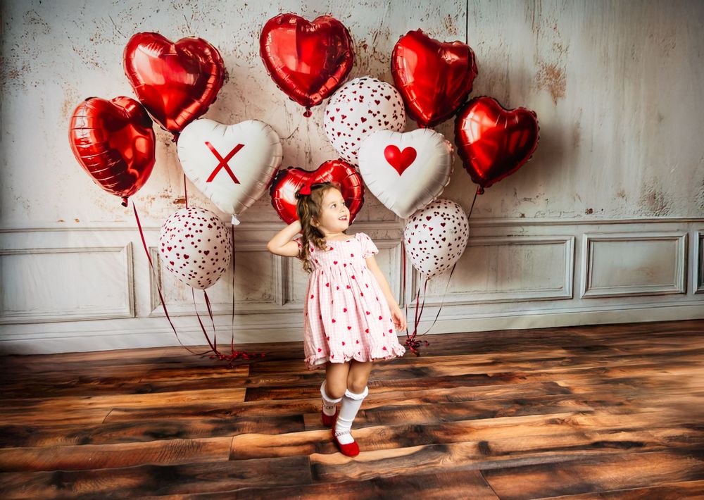 Valentine's photo scene with red heart balloons and polka dot white balloons against white wall and wooden floor.