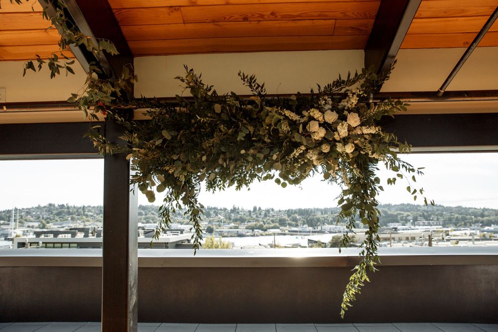 Elegant floral greenery installation hangs from wooden beams with waterfront view.
