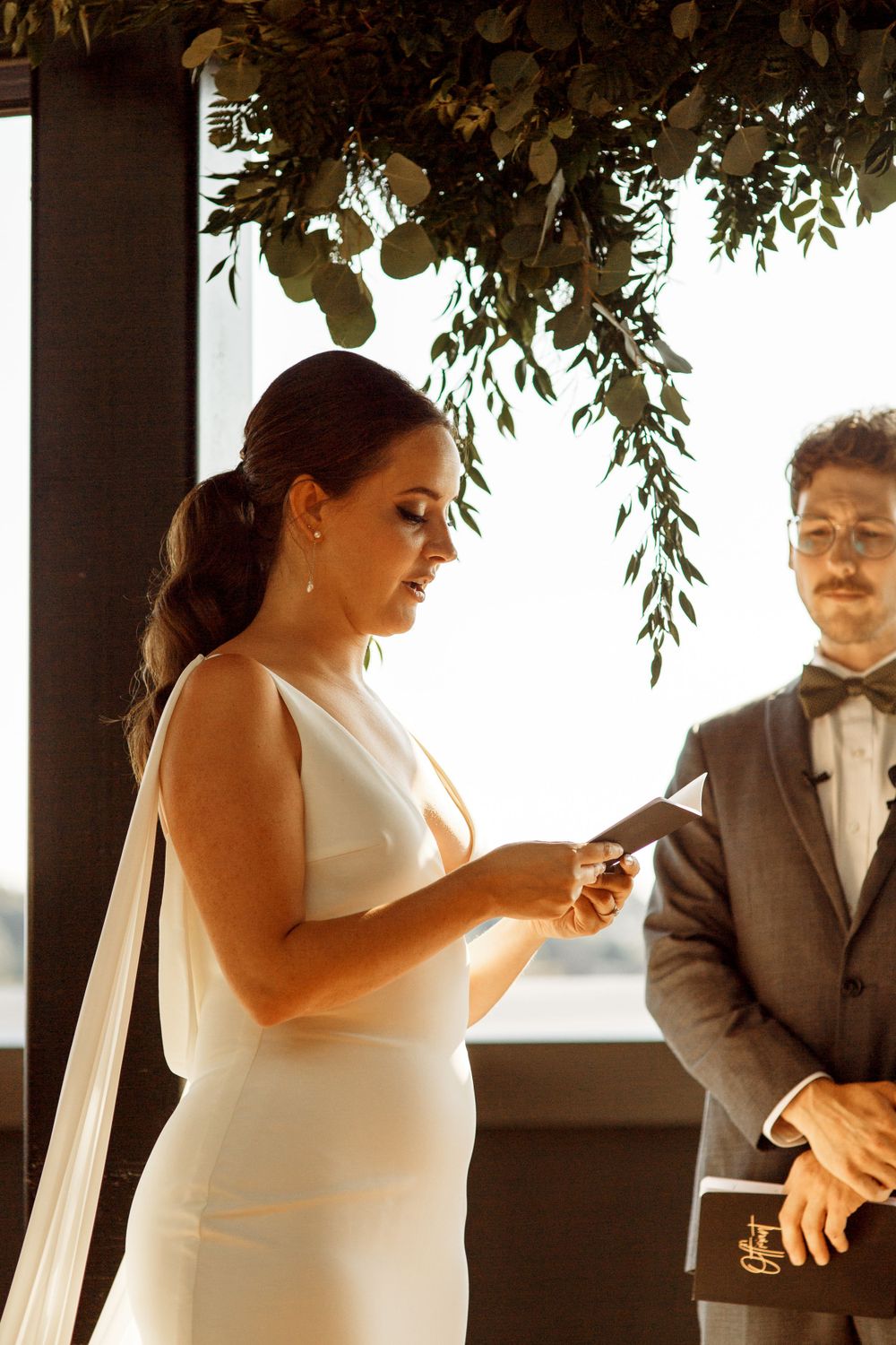 Wedding ceremony under hanging greenery decorations at an elegant indoor venue.