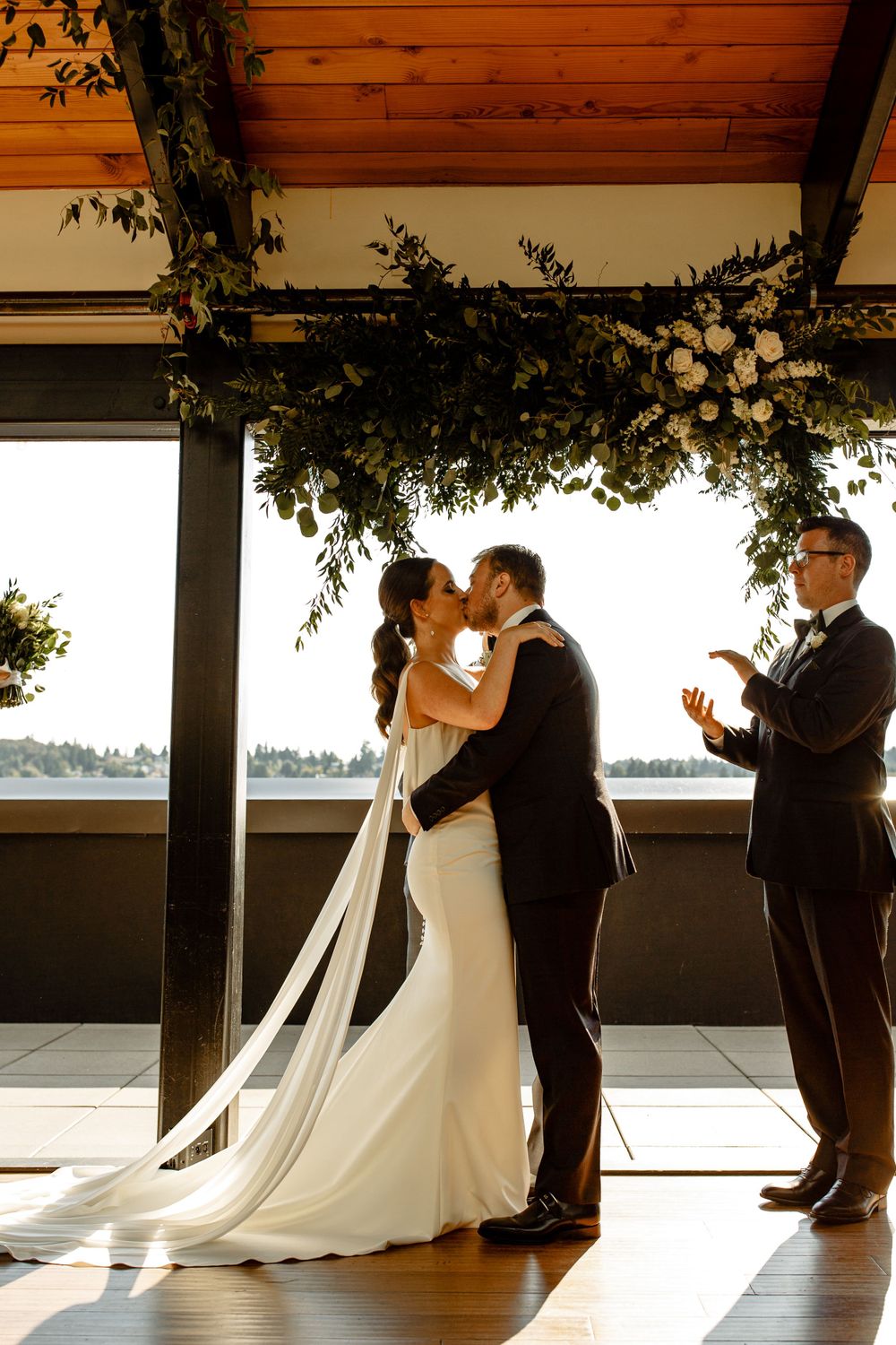 Wedding ceremony moment under decorative greenery garlands with waterfront views.