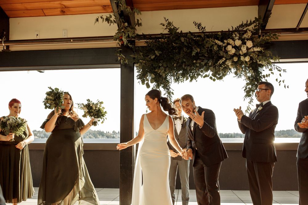 Wedding party celebrates during ceremony under wooden beams decorated with greenery.
