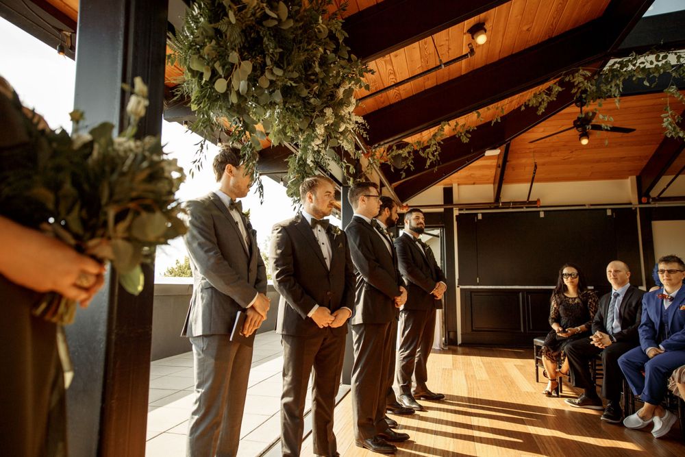 Wedding ceremony setup with wooden beams and hanging greenery overlooking scenic view.