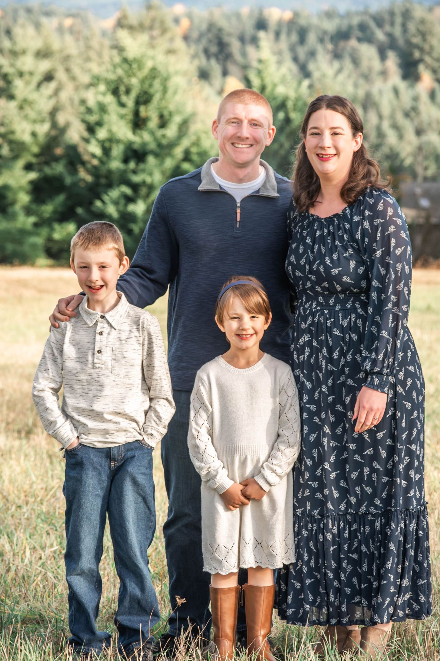 A family of four poses together outdoors in a grassy field on a sunny day.