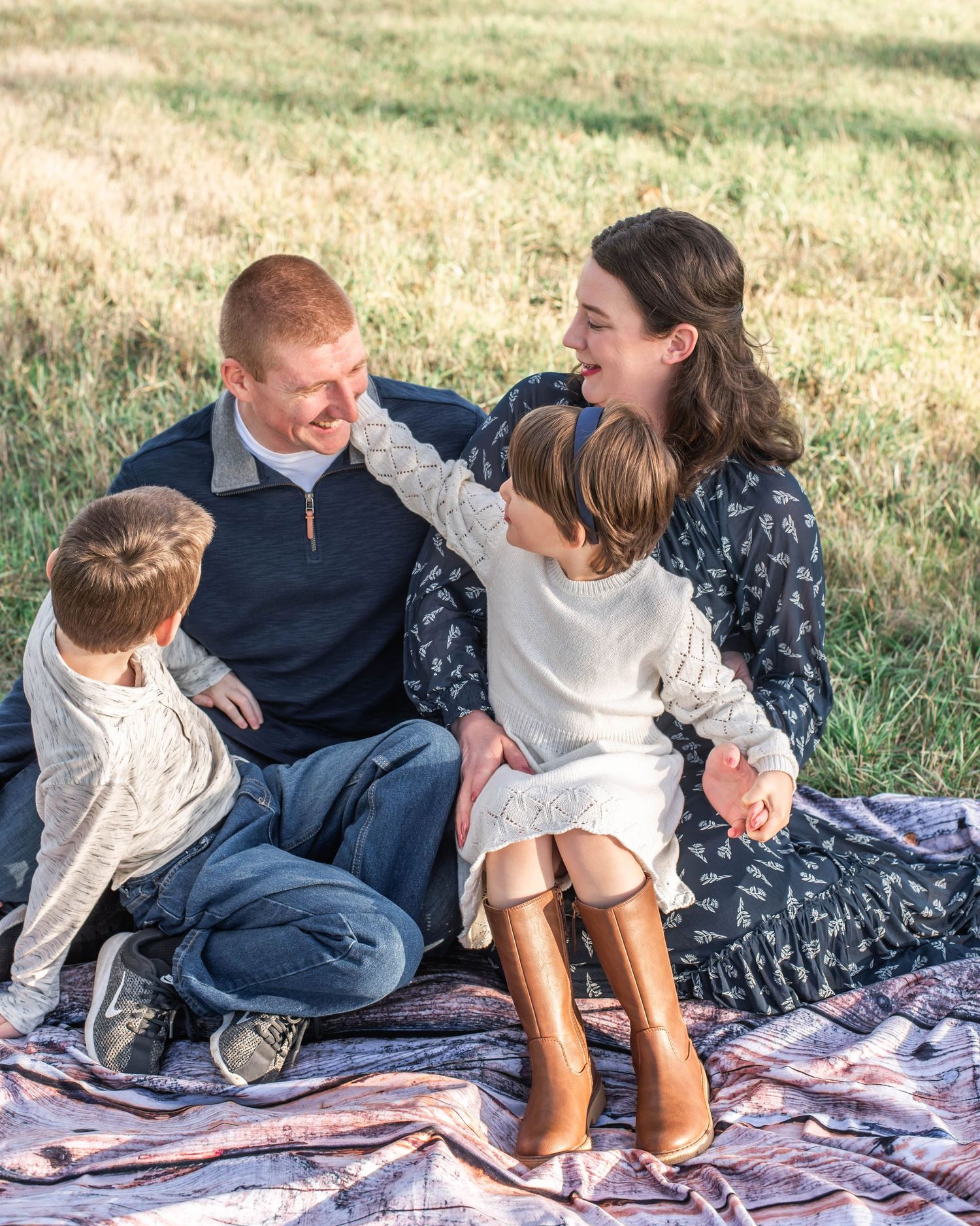 A family shares tender moments while relaxing together on a picnic blanket in a grassy field.
