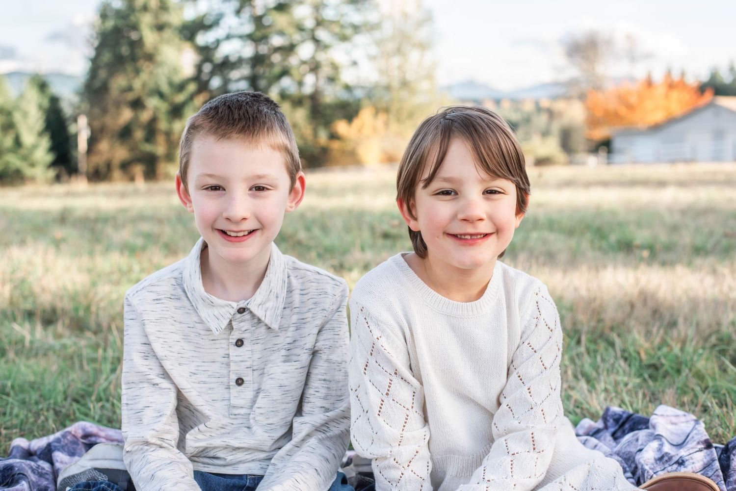 Two children sit together on a blanket outdoors during golden hour in autumn.