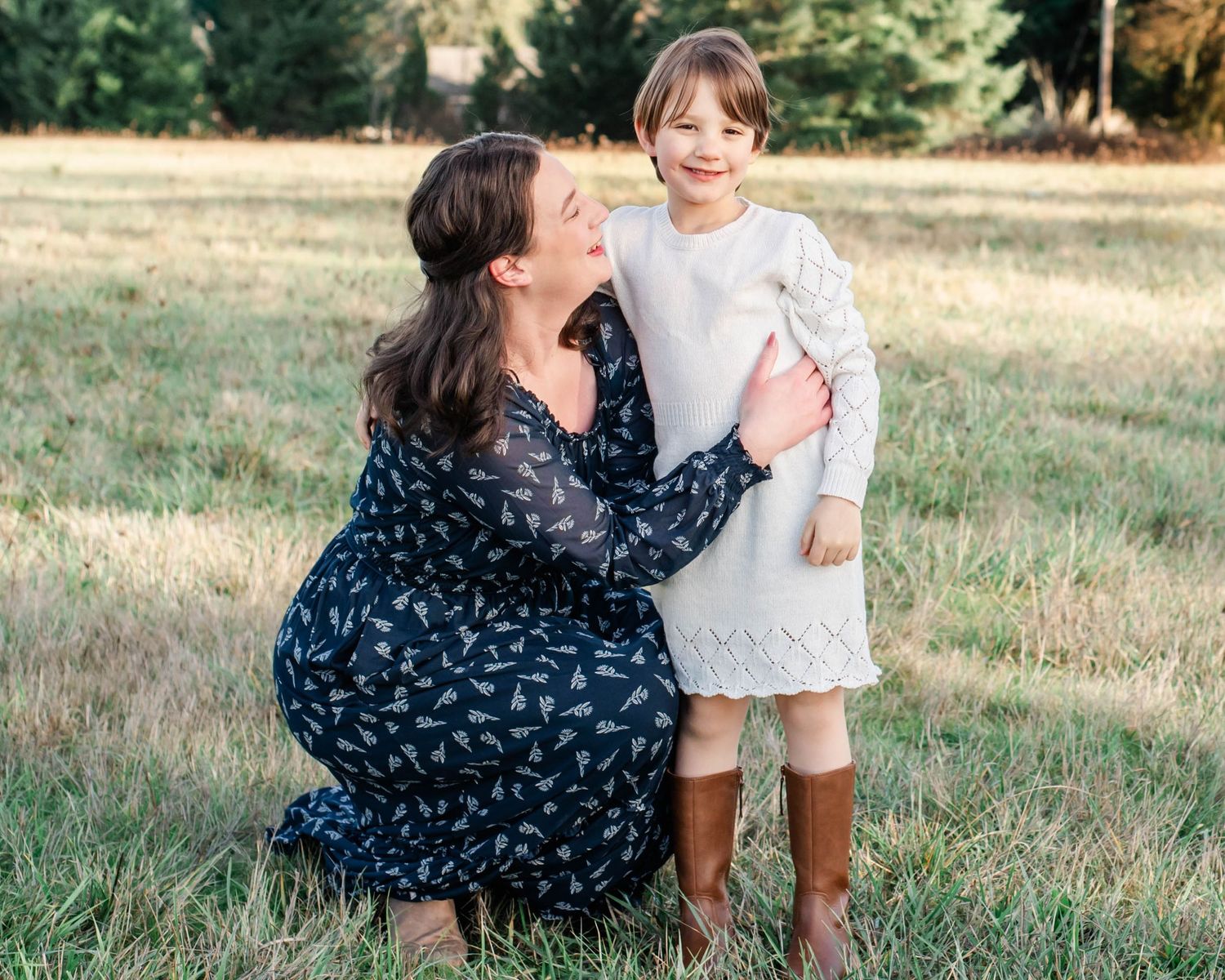 A touching outdoor family moment captured in a grassy field with fall foliage in the background.