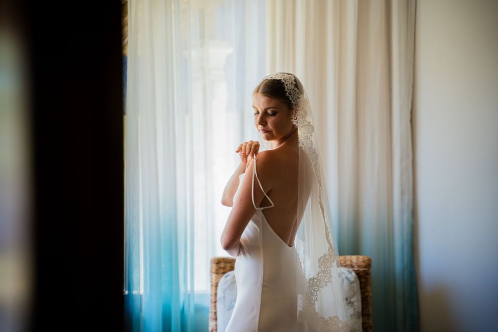 Artistic silhouette of a bride against white curtains in natural light.