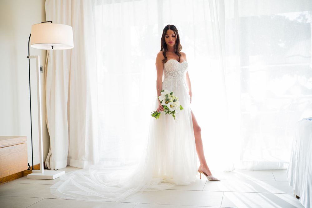 A sunlit bridal portrait in an elegant white room with flowing curtains.