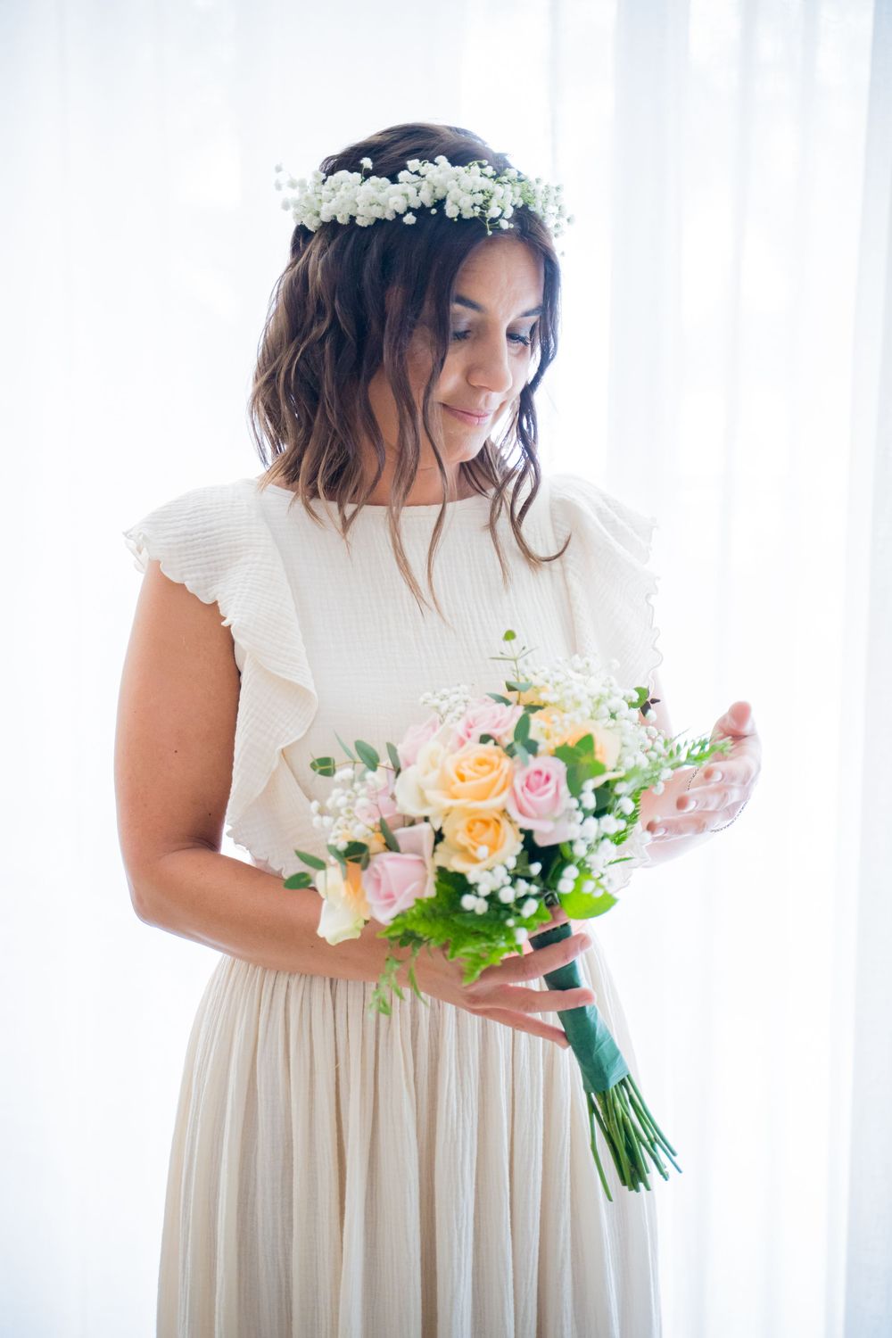 A romantic bridal portrait featuring a white dress and peach floral bouquet against bright windows.