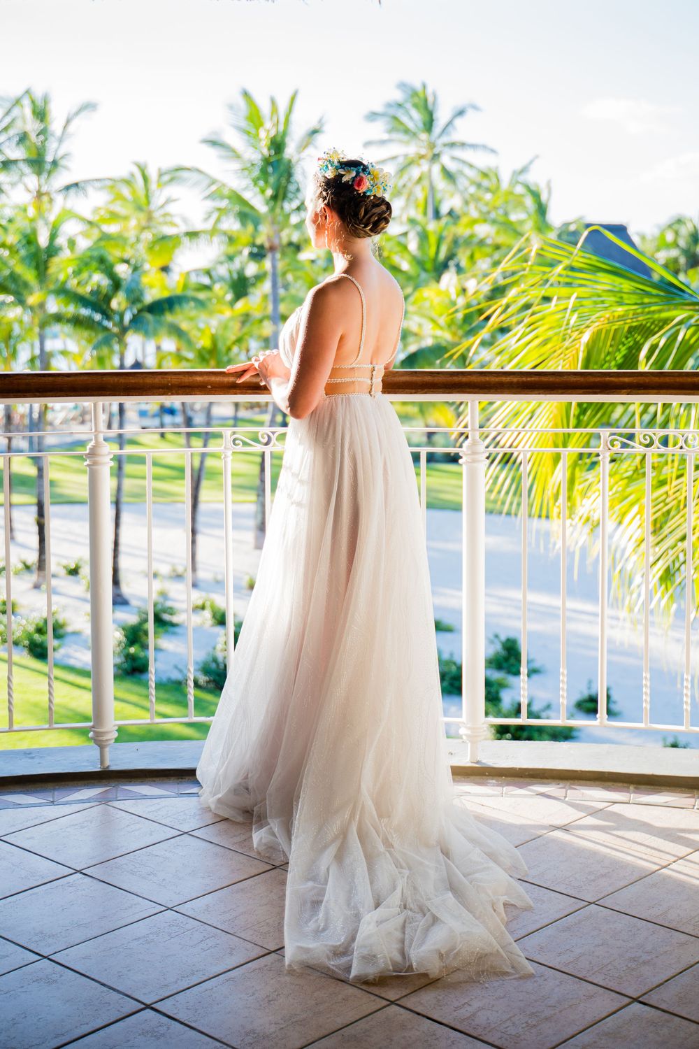 A flowing white wedding dress captured on a tropical balcony overlooking palm trees and ocean views.