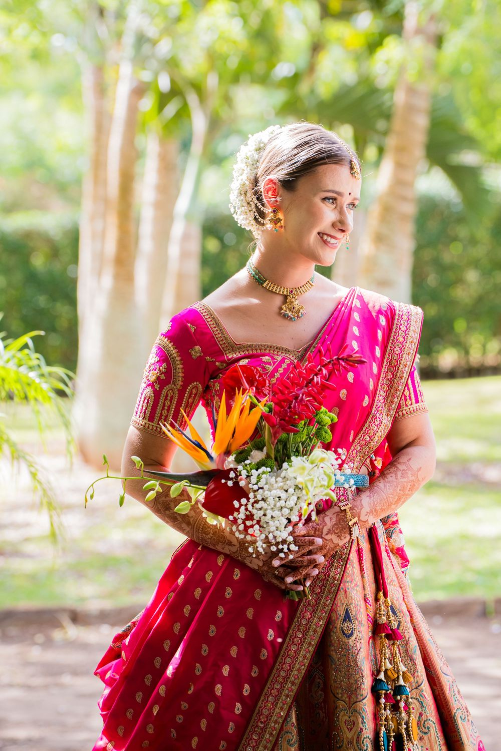 A stunning red and gold traditional Indian bridal lehenga displayed in a garden setting with vibrant floral details.