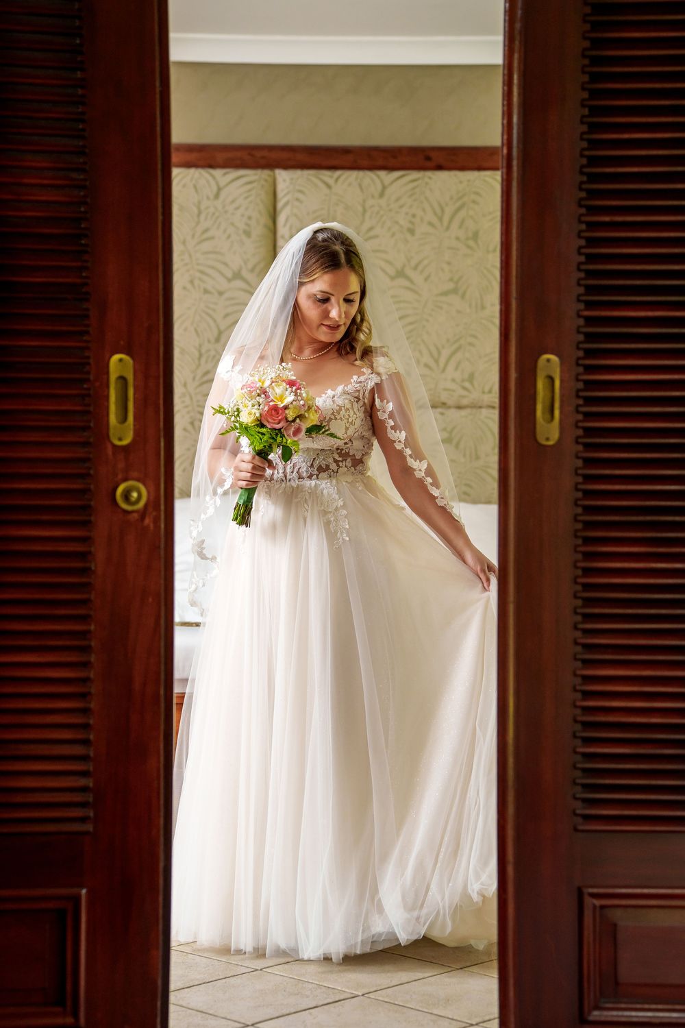 An elegant white wedding gown with delicate lace details shown through wooden door frames.