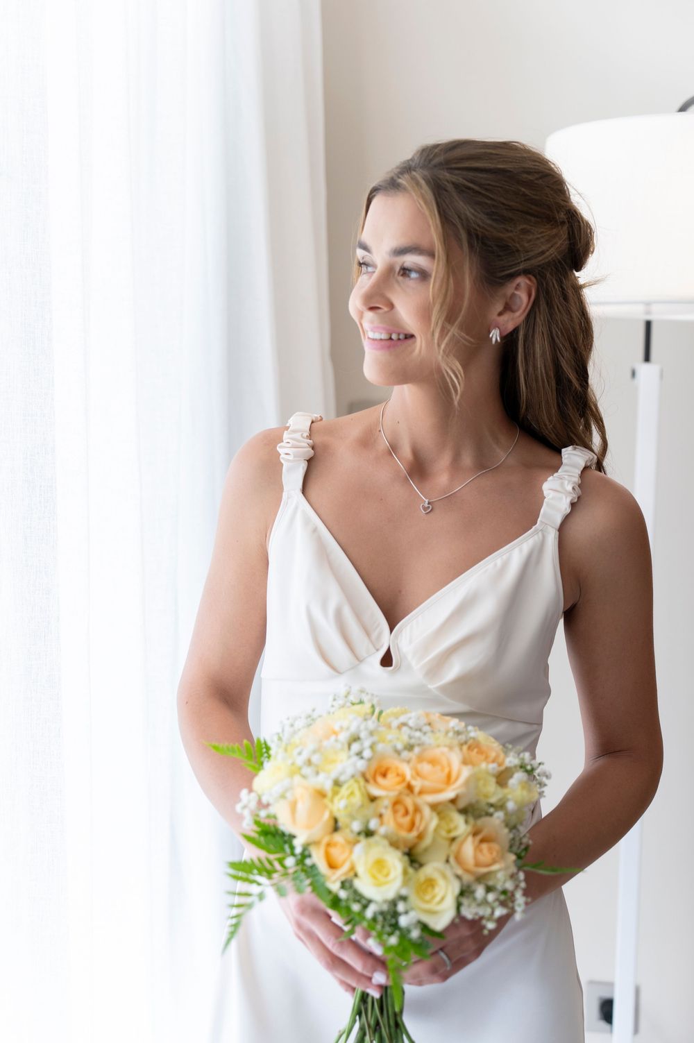 A joyful bridal portrait featuring a white dress with ruffled straps and peachy rose bouquet.