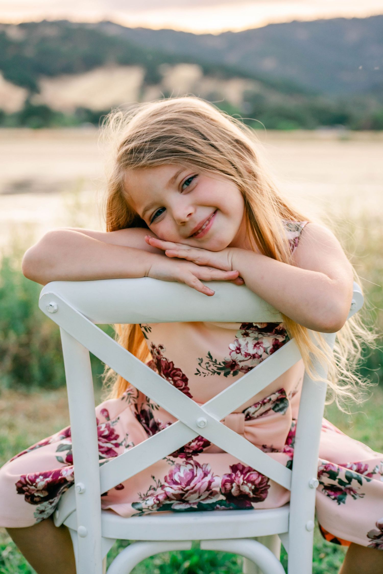 Dreamy outdoor portrait series of someone resting on a white wooden chair against a soft sunset background.