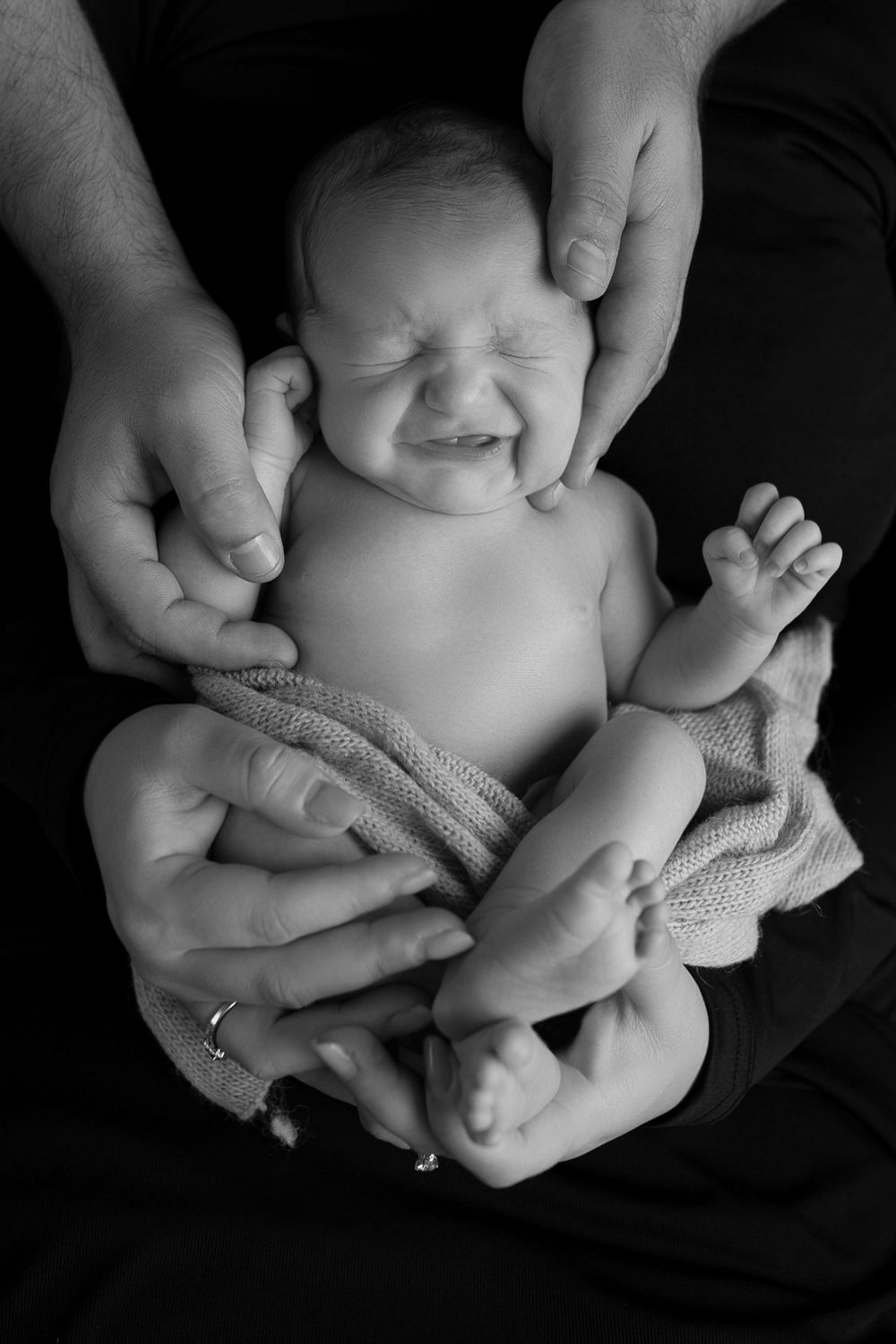 Black and white photo series showing gentle hands cradling a newborn baby wrapped in soft knit fabric.