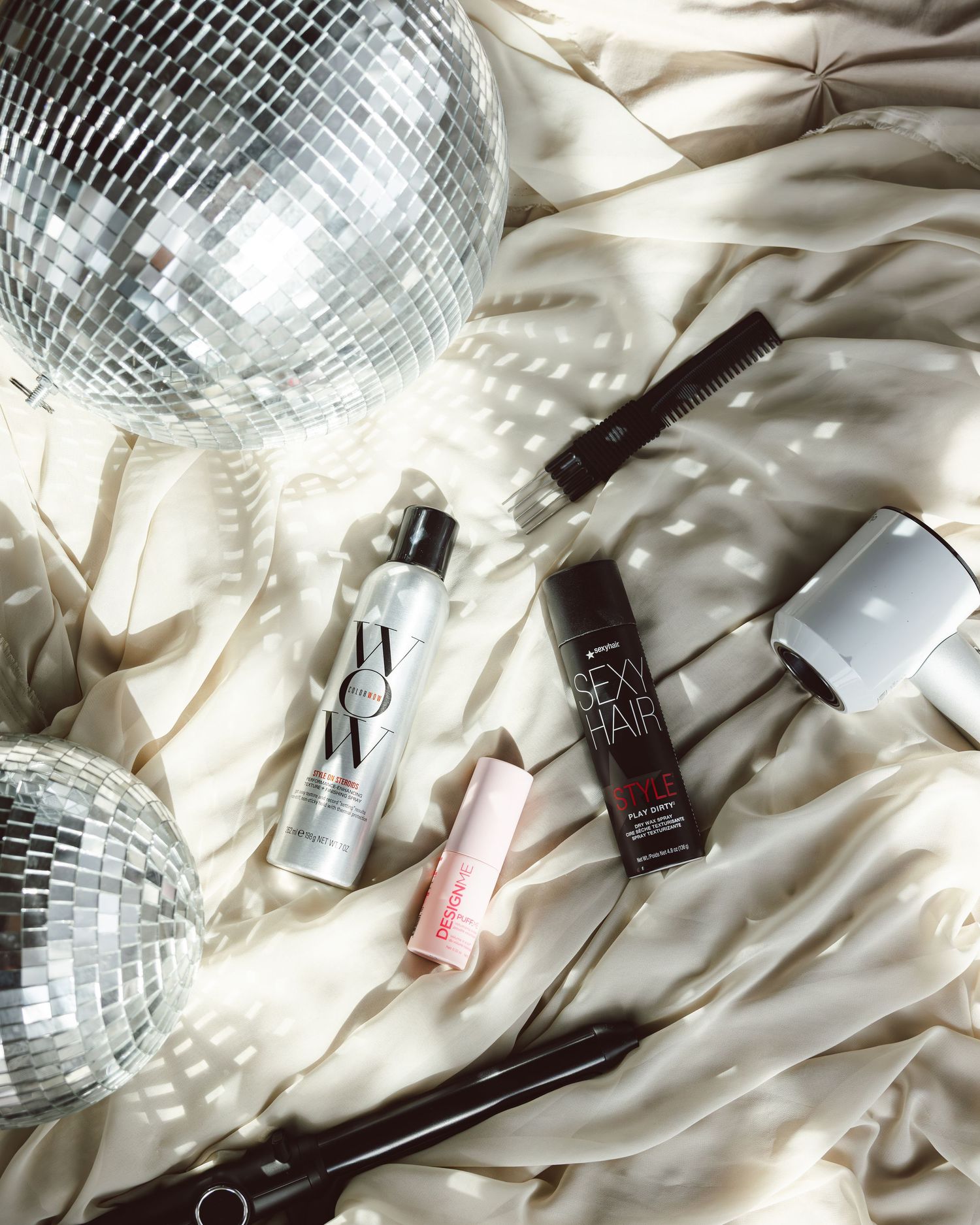 Disco ball reflecting light onto white bedding with beauty and fashion products scattered below.