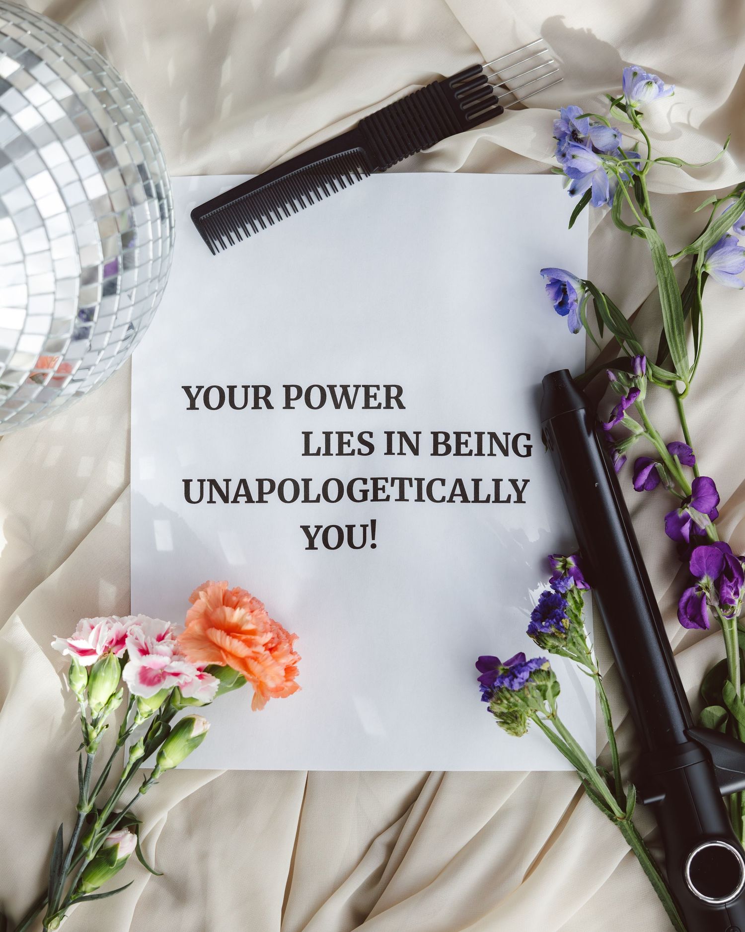Inspirational quote cards with 'Your Power' text arranged among purple flowers and hair styling tools on white fabric.