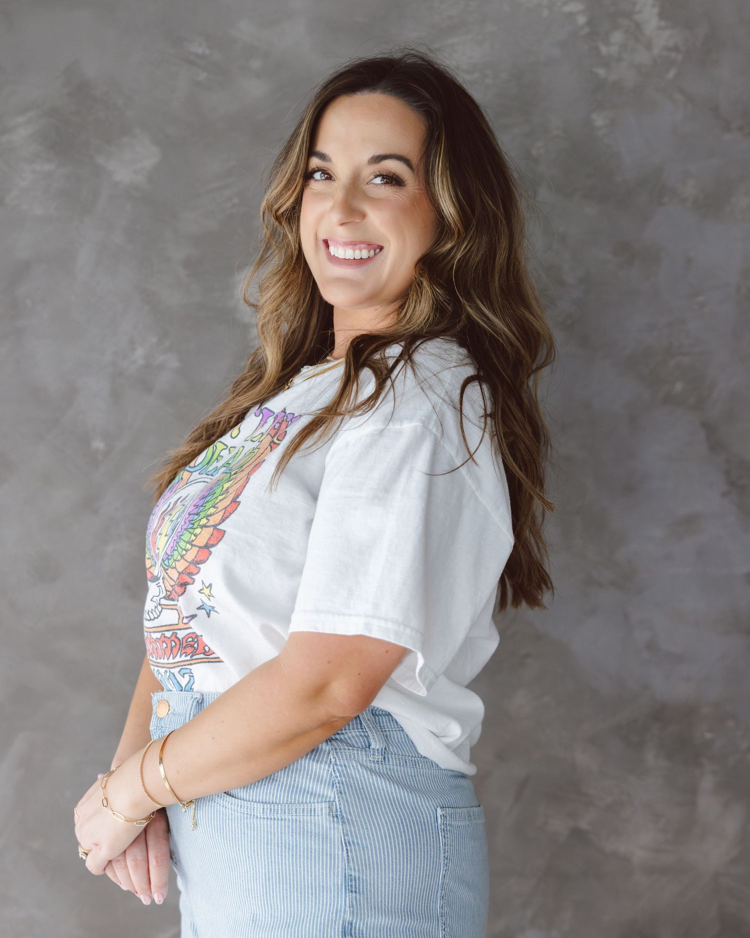 Person wearing white shirt and light denim poses against textured gray wall.